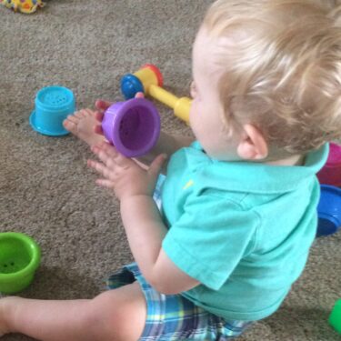 Toddler boy sitting on floor playing with colorful stacking cups