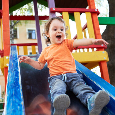 Young boy laughing while going down a slide outside
