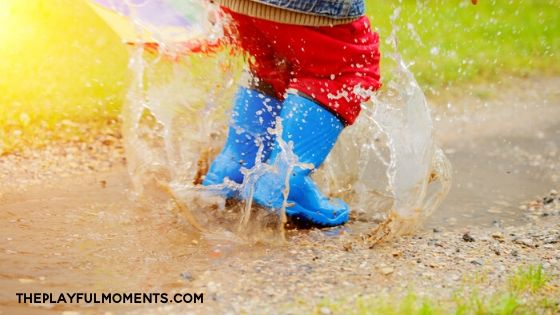 Child jumping in muddy puddle with boots