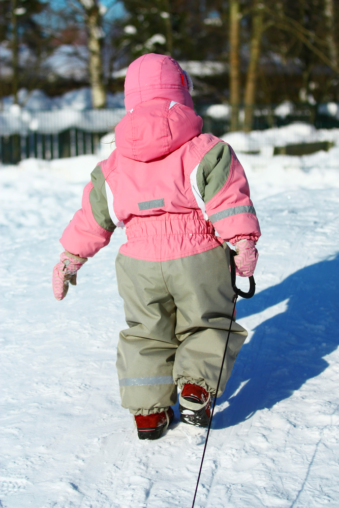 Child in snowsuit pulling sled up hill in the snow