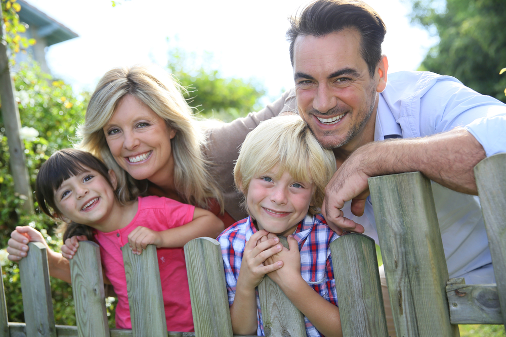 Mother, father, son and daughter smiling and leaning on wooden fence