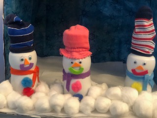 Three snowmen made out of white plastic bottles sitting on white felt surrounded by cotton balls