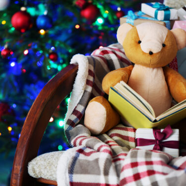 Teddy Bear reading a holiday book for kids on rocking chair by Christmas tree